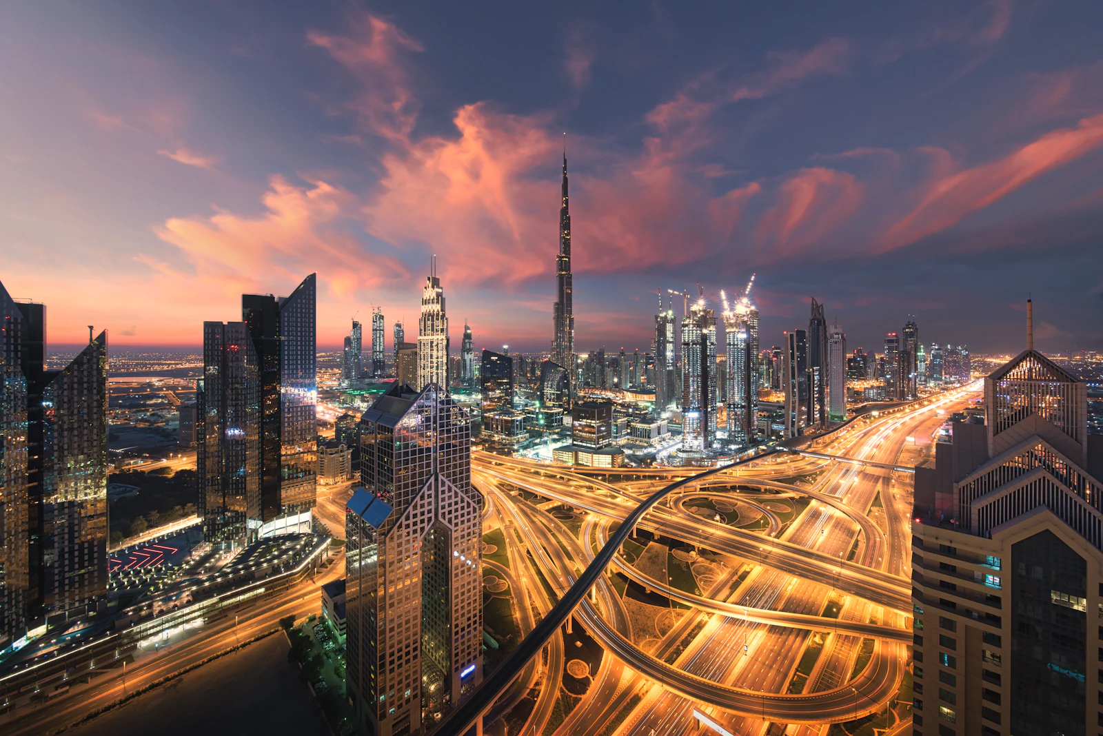 Downtown Dubai at dusk: the Burj Khalifa above lit towers and looping highway interchanges.